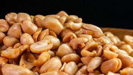 Close-up of a pile of roasted peanuts in a wooden plate on a dark background, suitable for snack, healthy food or culinary concepts.