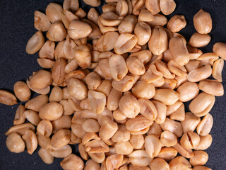 Top view roasted peeled peanuts scattered over a textured dark background. Suitable for snack themes, food illustrations, or ingredient stock photos.
