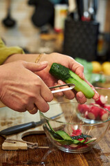 Side close-up of a woman peeling a cucumber in the kitchen to prepare a salad