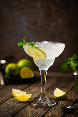 Cocktail margarita garnished with lime and mint on wooden background