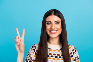 Portrait of a smiling happy woman showing victory v sign isolated blue pastel color background