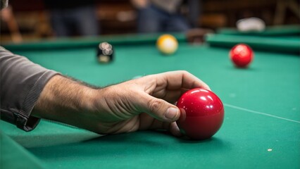 Man holding red billiard ball over table in dim lighting.