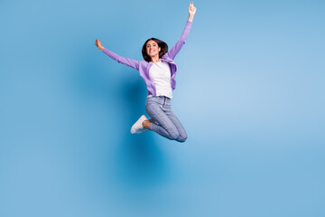 Fototapeta premium Full length view of attractive cheerful girl jumping having fun rising hands up isolated on blue color background