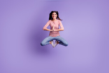Full body view of attractive cheerful girl jumping having fun having yoga training isolated on purple color background