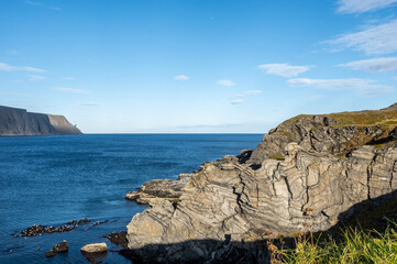  Dramatic rock formations and coastal cliffs at Kirkeporten viewpoint near Skarsvåg, Norway, close to North Cape. Stunning geological patterns meet Arctic Ocean under a clear blue sky