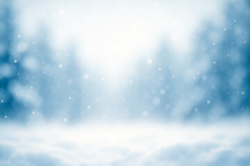Winter background with soft falling snow and blurry trees in blue tones.