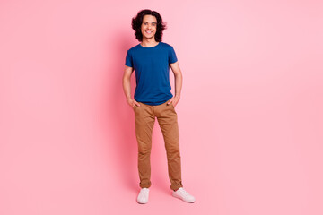 Full body photo of young guy posing holding hands in pants pockets isolated pink background