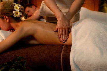 Fototapeta premium Caucasian couple customer enjoying relaxing anti-stress spa massage and pampering with beauty skin recreation leisure in warm candle lighting ambient salon spa at luxury resort or hotel. Quiescent