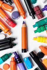 Vibrant art supplies arranged on a white background. A purple-tipped orange pencil stands out among colorful markers and stationery. Top-down view.