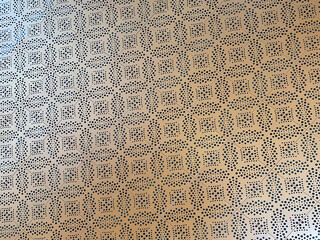 Texture of an iron plate with a repetitive laser cut pattern of squares and small dots, creating a hollow and industrial visual effect.
