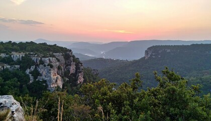 Fototapeta premium View of a valley with rocky cliffs and dense green trees under a beautiful sunset sky at dusk time