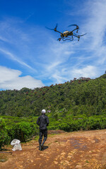 Flying industrial drone over a tea plantation in Nuwara Eliya, Sri Lanka, Asia. Image of an agricultural drone carrying a tank of liquid fertilizer.