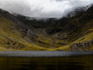 A tranquil mountain lake reflects the imposing cliffs shrouded in mist, evoking a sense of awe and solitude.