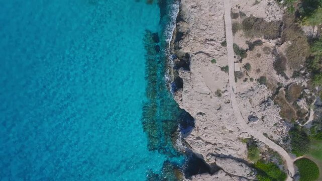 Aerial footage of Ayia Napa, Cyprus, showing turquoise waters, rugged rocky cliffs, pathways, and sparse vegetation along the coastline.