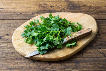 Fresh parsley on wooden cutting board with knife, organic herb preparation for cooking and healthy food recipes