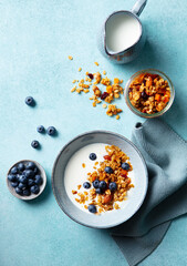 Healthy breakfast. Oat granola with fresh blueberries and milk in a bowl. Blue background. Close up. Top view.