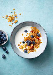 Healthy breakfast. Oat granola with fresh blueberries and milk in a bowl. Blue background. Top view.