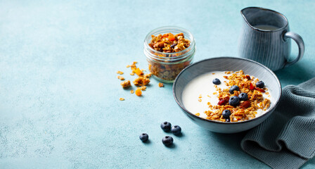 Healthy breakfast. Oat granola with fresh blueberries and milk in a bowl. Blue background. Copy space.