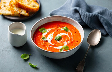 Tomato soup with cream and basil leaf in a white bowl on grey background. Close up.