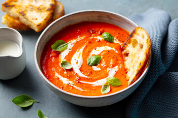 Roasted Tomato Soup with cream in a white bowl. Grey background. Close up.