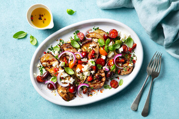 Grilled eggplants salad with feta cheese and tomatoes on a plate. Blue background. Top view.