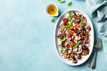 Grilled eggplants salad with feta cheese and tomatoes on a plate. Blue background. Copy space. Top view.