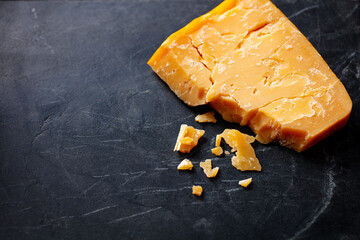 Cheddar cheese on black marble cutting board. Dark background. Copy space. Close up.