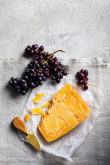 Aged cheddar cheese with knife on parchment paper. Grey background. Copy space. Top view.