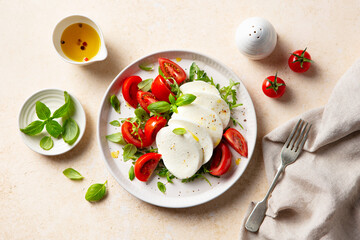 Traditional Italian cuisine. Caprese salad with tomatoes, mozzarella cheese and fresh basil. Beige background. Close up. Top view.