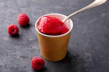 Refreshing raspberry sorbet in a paper cup. Slate background. Close up.