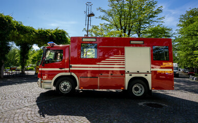 Bright Red Fire Truck Parked on a Cobblestone Street Surrounded by Green Trees on a Clear Sunny Day