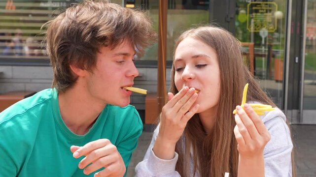 Cute Caucasian teen lovers boy and girl or friends eating fast food burgers and fries in a restaurant.