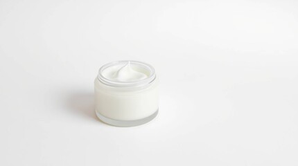A small glass jar filled with a white, creamy substance, resembling lotion or moisturizer, sits on a white background