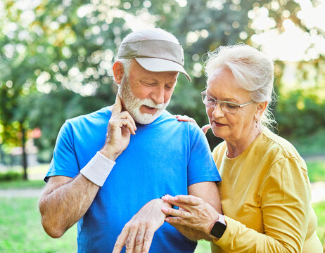 Smiling active senior couple jogging exercising and having fun and laughing together taking a break in the park, senior athletes checking their er heart rate with smartwatch - Powered by Adobe