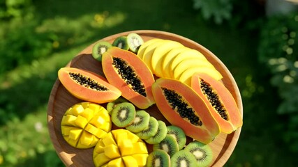 Fruit platter paradise mango cubes papaya halves  kiwi slices on wood bathed in sunlight against a green backdrop - Powered by Adobe