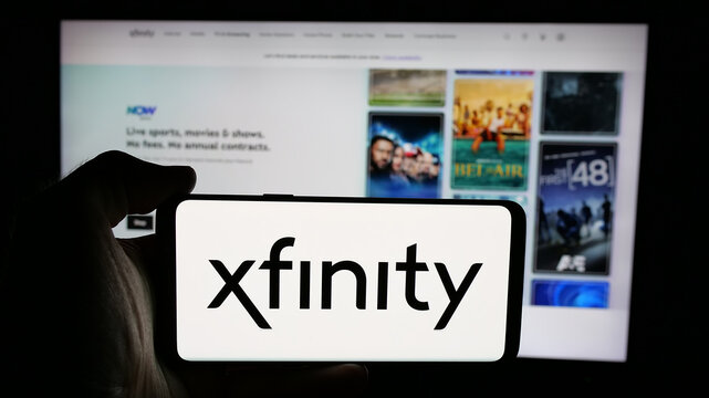 Stuttgart, Germany - 05-18-2025: Person holding cellphone with logo of Comcast Cable Communications LLC (Xfinity) on screen in front of webpage. Focus on phone display.