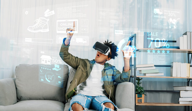 Smart african man with VR glasses buying product and accessing online market. Happy person shopping and sitting on sofa while checking at discount from online market hologram. Technology. Ingenuity.