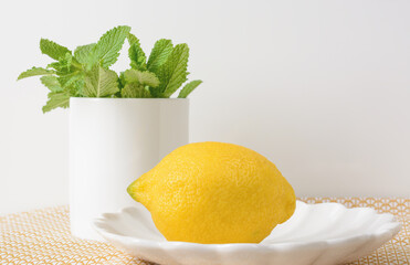 Lemon lying on a saucer on a light background with mint leaves in a white mug, selective focus