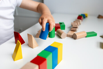 Child playing with colorful geometric wooden blocks on white surface