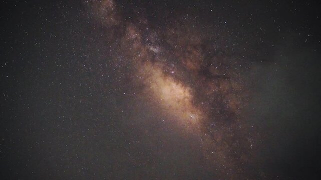 A stunning timelapse of the Milky Way galaxy illuminating the night sky as wispy clouds drift gracefully across the frame. The stars appear to rotate due to Earth's natural movement.