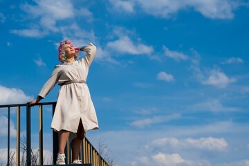 A woman with colored hair walks outdoors. Portrait of a girl against the blue sky. 