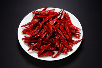Heap of dry red chilies over white ceramic plate isolated on dark background close-up view 