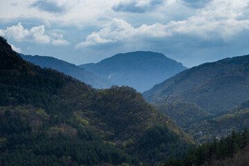 Layered Mountain Ridges and Forest Valleys Fade into Blue Distance Under Cloud-Filled Sky