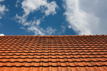 Classic red tiled roof under a bright blue sky with scattered clouds. Traditional European roofing captured in clean, geometric perspective