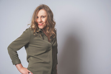 Smiling, happy middle-aged woman with blonde hair in green shirt. Portrait to the waistб gray backgound