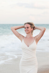 Beautiful young happy blonde girl in a white short dress on the sea on the beach in summer. Photo model. Model. Posing.