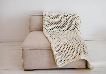 Cozy modern sofa with knitted blanket draped over it in a minimalistic interior setting