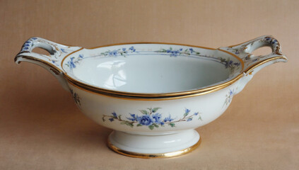 Elegant porcelain serving bowl with floral design and gold accents, featuring two handles, displayed on a soft beige background, ideal for dining and decorative purposes