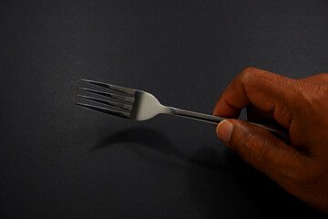 hand holding a fork  with black background closeup view selective focused 