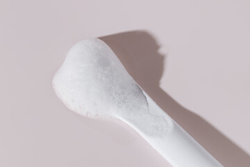 Foamy cleanser on white spatula, pastel pink background.